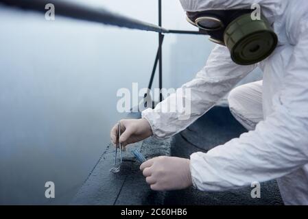 Employé de laboratoire en culture, recueillant des échantillons à l'aide de pinces pour analyse dans les zones contaminées, par temps brumeux gris, vue de près Banque D'Images
