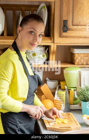 Jolie jeune femme au foyer en tablier noir pose dans la cuisine de maison de campagne en bois Banque D'Images