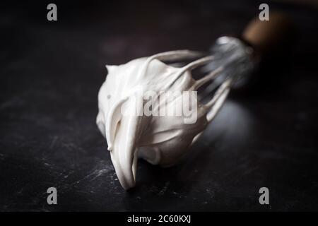 Fouet à main avec mélange de meringue blanc d'œuf battu. Gros plan sur fond noir. Banque D'Images