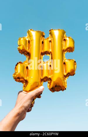 gros plan de la main d'un jeune homme caucasien tenant un ballon d'or en forme de symbole de hash contre le ciel bleu Banque D'Images