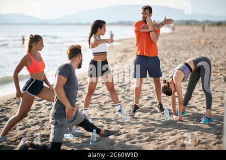 groupe caucasien de deux hommes et trois femmes s'étirant, se réchauffant pour faire de l'exercice à la plage Banque D'Images
