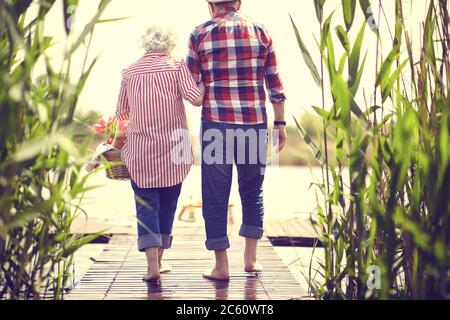 Un couple de personnes âgées aimant se rend sur l'étang au pique-nique. Des personnes âgées heureuses au pique-nique. Banque D'Images