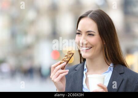 Bonne femme de direction tenant une tasse de café à emporter et un bar à céréales dans la rue Banque D'Images