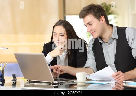 Les employés de bureau satisfaits vérifient le contenu en ligne de leur ordinateur portable au bureau Banque D'Images