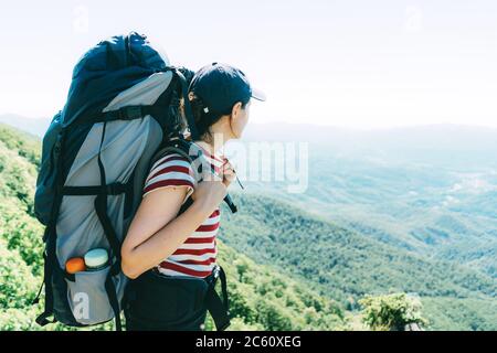 Une femme touriste avec un grand sac à dos de camping sur une expédition se tient sur le dessus et regarde le paysage. Banque D'Images