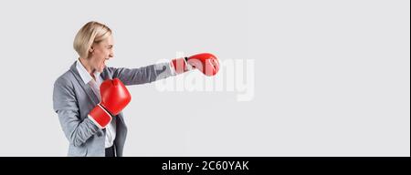 Vue latérale de la femme d'affaires en gants de boxe, punch sur fond clair, panorama avec espace vierge Banque D'Images