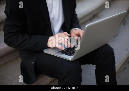 Homme d'affaires en gros plan dans un costume classique travaillant sur un ordinateur portable extérieur Banque D'Images