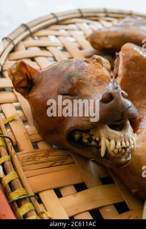 Gros plan sur la tête de chien rôtie, viande de partie du corps à vendre sur le marché de rue, sur plateau en osier dégoûtant la nourriture locale vietnamienne. Hanoï, Vietnam Banque D'Images