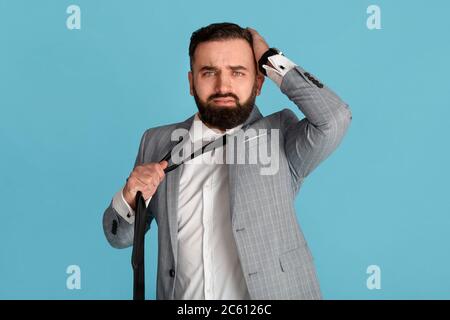 Homme d'affaires en tenue de cérémonie tenant sa tête et cravate dans le désespoir sur fond bleu Banque D'Images