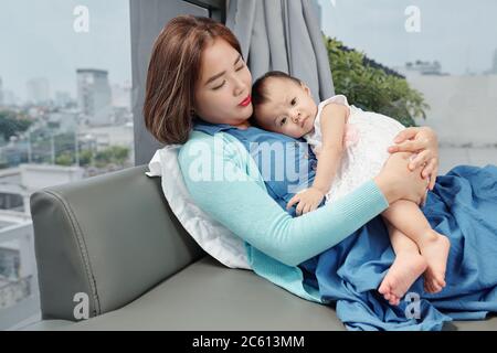 Jolie jeune femme vietnamienne reposant sur un canapé avec une petite fille sur la poitrine Banque D'Images