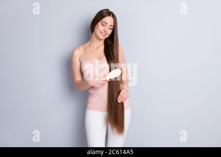 Photo de l'apparence parfaite modèle attrayant femme long coiffure tenir peigne en bois préféré brossant les boucles fortes portent un pantalon singlet beige isolé Banque D'Images