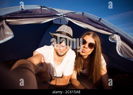 Camping drôle de couple en tente prenant selfie. Des amis heureux qui s'amusent à togheter. Concept de mode de vie actif et de technologie Banque D'Images