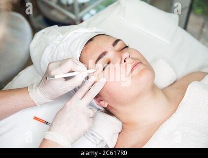 Les mains des médecins en gants touchent le visage de la femme. Procédure anti-froissage Banque D'Images