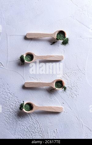 Poudre de chlorelle ou de spiruline verte naturelle dans quatre petites pelles en bois organisées verticalement. Concept de nourriture saine et de régime. Texte blanc Banque D'Images