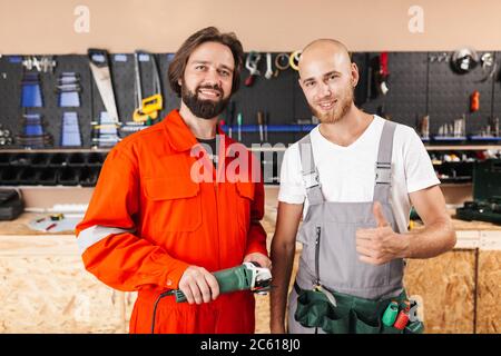 Deux fabricants souriants dans les vêtements de travail regardant avec plaisir dans les appareils photo s. Banque D'Images