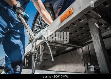 Travailleur caucasien fixant la voiture sur un camion de remorquage à l'aide de ceintures d'arrimage. Thème transport et fret. Banque D'Images