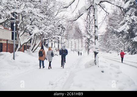 Les rues de la ville après le blizzard de la tempête de neige hivernale. Les cyclistes passent et les piétons marchent en hiver sur la rue enneigée Banque D'Images