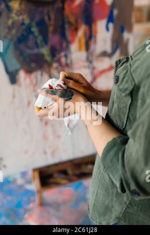 Photo de la femme mains dans les peintures tenant une photo de dessin de serviette blanche sur toile avec des peintures à l'huile dans l'atelier Banque D'Images