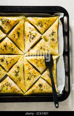 samosa indien à base de phyllo avec pommes de terre épicées et légumes sur une plaque à pâtisserie, prêt à être cuit au four avec des graines de sésame noir Banque D'Images