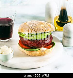 hamburger végétalien sans viande avec avocat, tomates et épinards sur la table et vin rouge dans un verre Banque D'Images