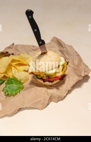 Hamburger végétalien avec légumes et chips de pommes de terre sur le côté. Servi sur du papier recyclé sur fond crème clair. Repas végétalien rustique, cuisine végétarienne r Banque D'Images