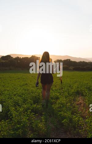 Jeune femme, marchant vers le coucher du soleil sur un terrain d'herbe, tenant un appareil photo d'époque et une bande de film. Hipster fille photographe, voyage et preservi Banque D'Images