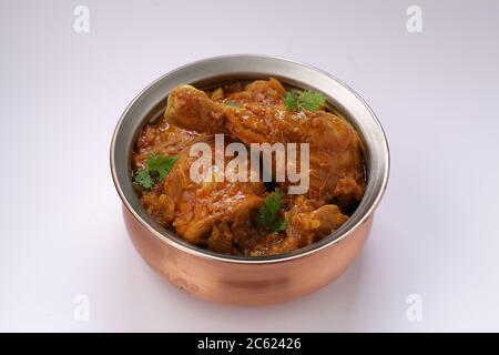 Curry de poulet ou masala, plat épicé de morceau de jambe de poulet rougeâtre garni de feuilles de coriandre, qui est traditionnellement disposé dans un bol en laiton Banque D'Images