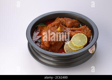 Curry de mouton ou curry d'agneau, épicé et délicieux plat garni de feuilles de curry et de tranches de citron dans un récipient noir à texture ou fond blanc, an Banque D'Images