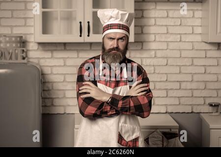 Beau chef cuisinier barbu en uniforme blanc et chapeau avec longue moustache luxuriante sur le visage sérieux debout et les mains jointes. Banque D'Images
