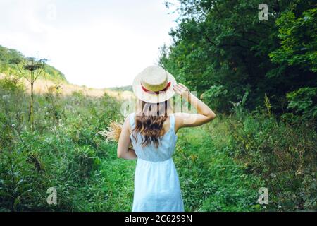 Jeune femme avec cheveux bouclés dans un chapeau. Fille mince dans un chapeau avec son dos tourné. Banque D'Images