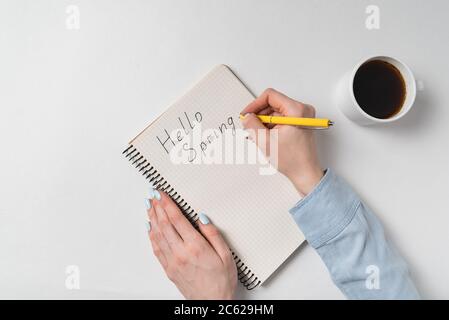 Bonjour printemps écrit sur le carnet sur fond blanc. Café du matin et nouvelles idées. Banque D'Images