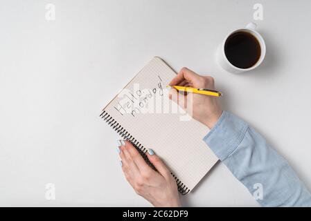 Les femmes écrivent dans le texte du Bloc-notes Bonjour lundi, tasse de café sur fond blanc. Vue de dessus. Banque D'Images