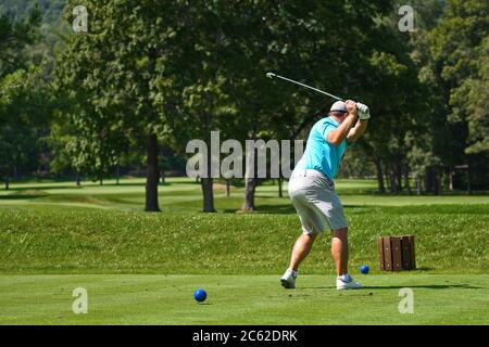 Jeune homme sur le parcours de golf en train de frapper un fer de la boîte à tee tout en jouant une partie de golf Banque D'Images