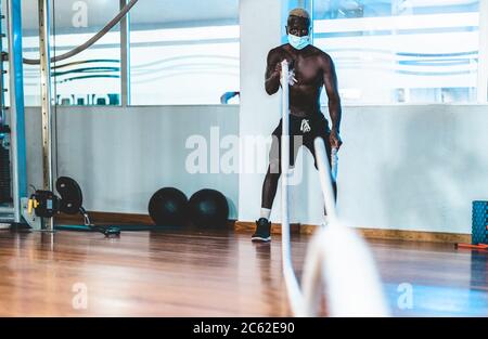 Jeune homme noir faisant une séance d'entraînement avec corde de bataille tout en portant un masque de visage pour la prévention du coronavirus - concept de santé, de forme physique et de sport - FO Banque D'Images