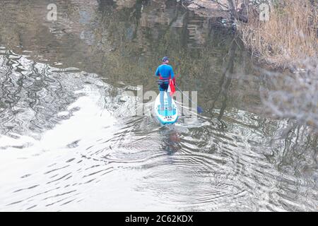 Vue de dessus des sportifs entraînés debout sur le stand-up paddle board et marchant sur l'eau calme de la rivière. Homme pagayant sur SUP dans la rivière. Banque D'Images
