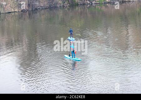 Vue de dessus des personnes formées debout sur les planches à aubes debout et marchant sur l'eau calme de la rivière. Homme pagayant sur SUP dans la rivière. Banque D'Images