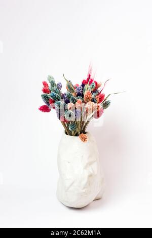 Lames d'herbe colorées dans un vase texturé sur fond blanc. Banque D'Images