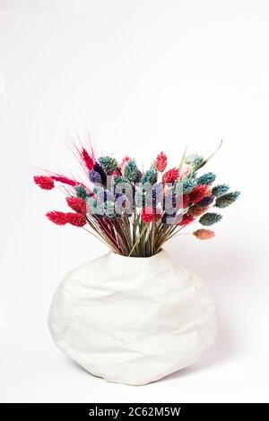 Lames d'herbe colorées dans un vase texturé sur fond blanc. Banque D'Images