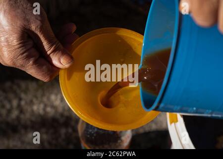 Old woman's hands pouring juice de la poêle en bouteille entonnoir via Banque D'Images