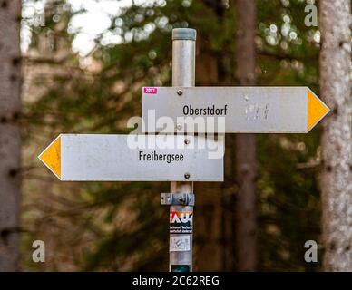 Un panneau indicateur dans la forêt montagneuse montre le chemin vers Oberstdorf et vers le Freibergsee, en Bavière, Allemagne. Banque D'Images