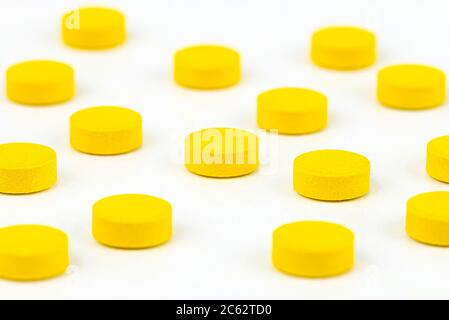 Prise de vue macro de comprimés jaunes disposés aléatoirement, isolés sur fond blanc. Banque D'Images