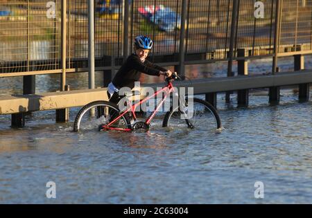 Un jeune garçon pousse son vélo dans les eaux d'inondation sur la route circulaire nord près de Brent Cross, au nord de Londres, après une explosion de la conduite principale d'eau. Banque D'Images