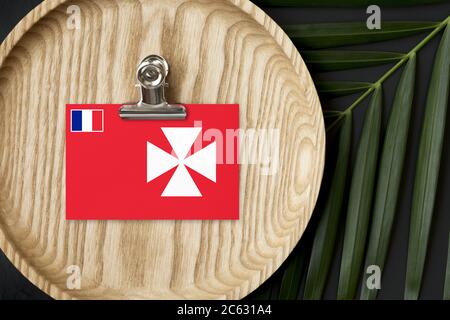 Drapeau Wallis et Futuna marqué sur une plaque de bois. Le palmier tropical laisse la monstère sur le fond. Concept national minimal. Banque D'Images