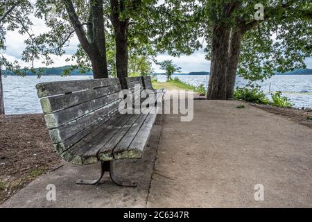 Trois bancs en bois assis au lac près du rivage pour se reposer et observer avec les arbres entourant le sentier par les bancs du parc sur un clin Banque D'Images