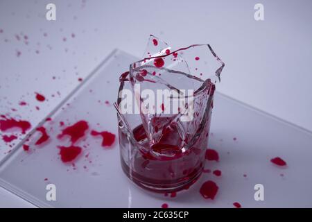 gouttes de liquide rouge - sang - sur les fragments d'un verre brisé dans un verre brisé sur un fond blanc. Isolé. Espace de copie. Concept de douleur. Photo de haute qualité Banque D'Images