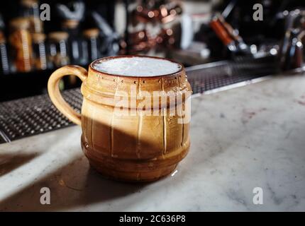 Bière artisanale froide dans une tasse en céramique avec une goutte de mousse. Tasse de bière légère sur un pub sombre Banque D'Images