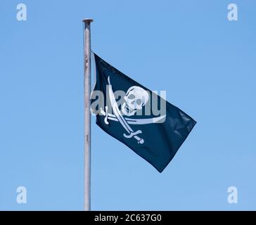 Drapeau de pirate Jolly Roger agitant contre le ciel bleu Banque D'Images