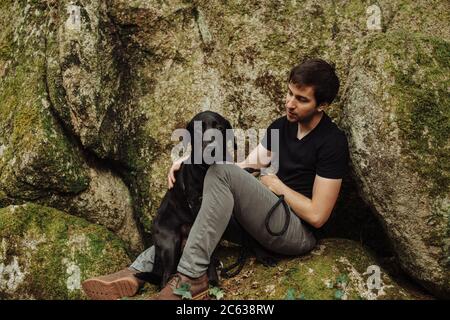 Jeune homme avec un Labrador noir retriever assis sur un roche mossy Banque D'Images