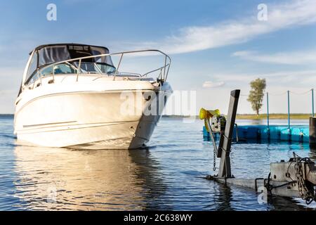 Grand luxe cabine bateau à moteur bateau de croisière yacht lancement à la rampe de remorque sur la rivière ou le lac. Lever de soleil chaud du matin reflet du soleil dans une surface d'eau calme Banque D'Images