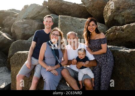 Une famille de cinq personnes souriant pour une caméra assise sur Rocks à Plage Banque D'Images